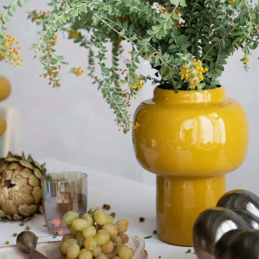 Yellow vase with greenery on a table with decorative items